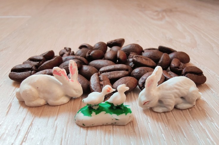 Pieniä muovisia pupuja ja lintuja kahvipapujen vieressä.