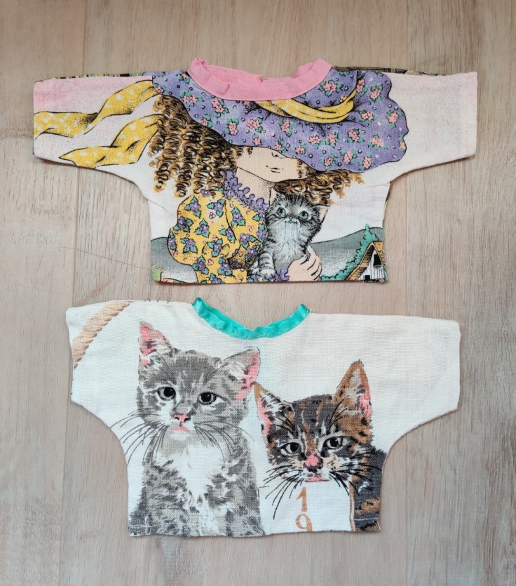 Kaksi itse tehtyä nuken puseroa. Toinen pusero on tehty 1980-luvun kangaskalenterista.