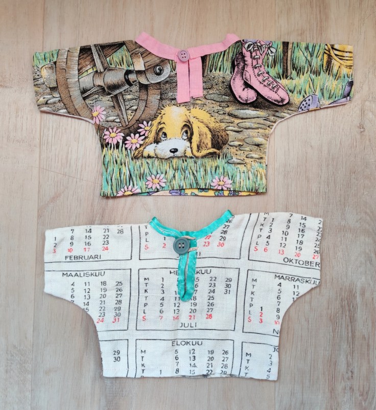 Kaksi itse tehtyä nuken puseroa selkäpuolelta. Toinen pusero on tehty 1980-luvun kangaskalenterista.