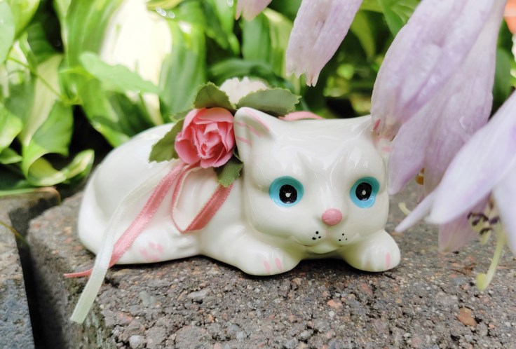 Valkoinen keramiikkakissa, figuurin selässä kangasruusu ja koristenauhoja.