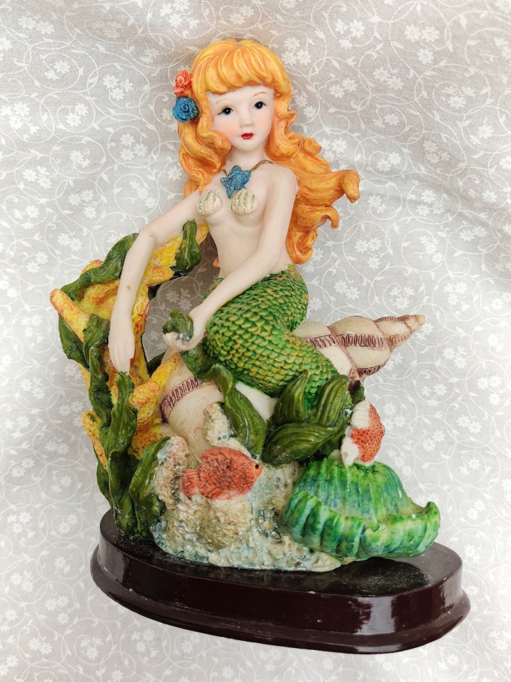 Merenneitofiguuri simpukan päällä, kiinnitetty puualustalle.