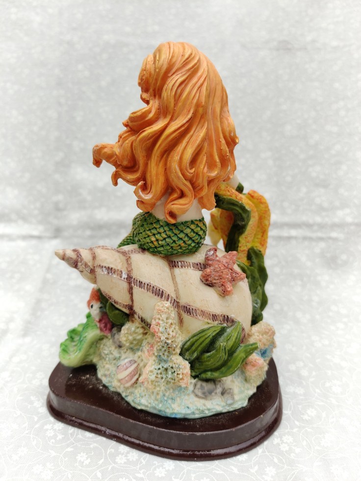 Merenneitofiguuri simpukan päällä, kiinnitetty puualustalle. Figuurin selkäpuoli.