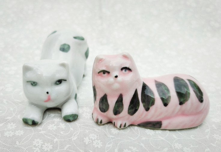 Venyttelevä keramiikkakissa ja makaava keramiikkakissa.