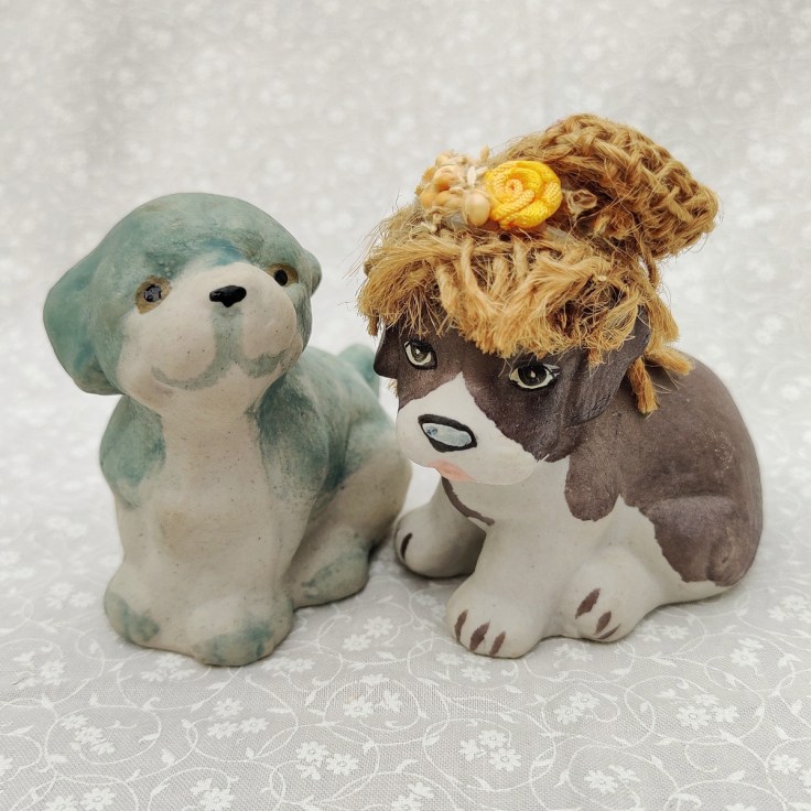 Kaksi keramiikkakoiraa, toisella kangashattu päässä.