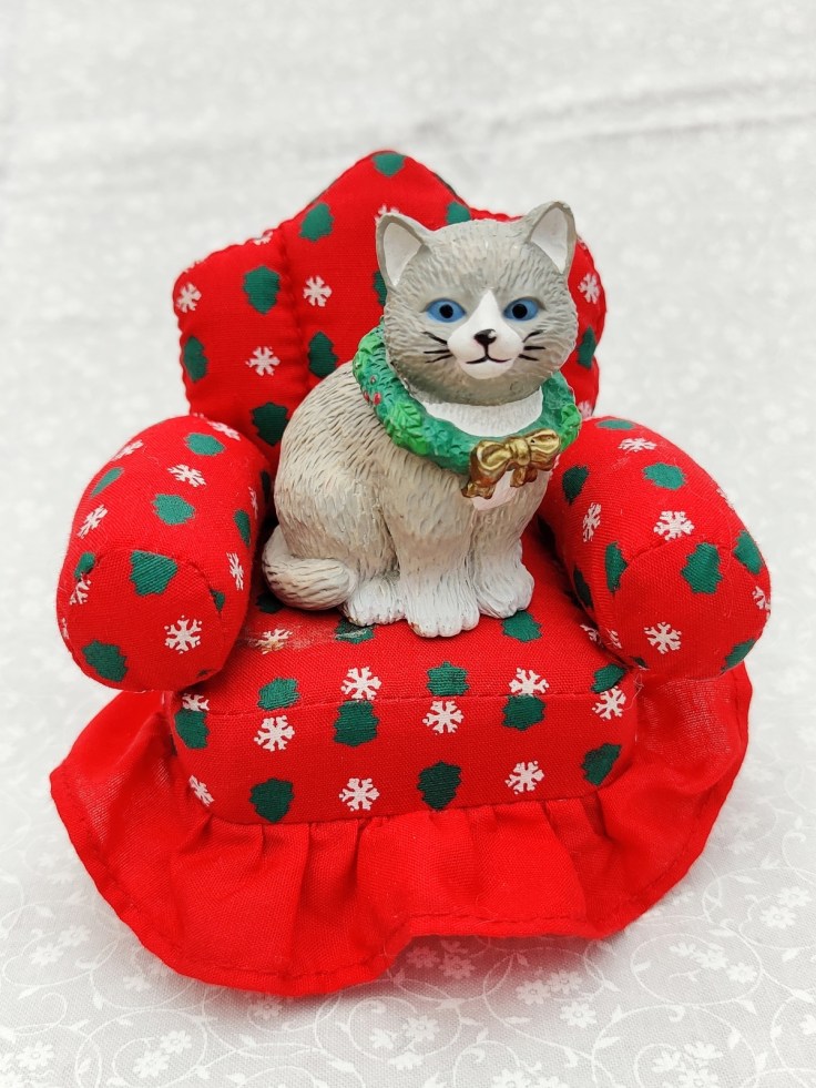 Jouluaiheinen kissafiguuri pienen nojatuolin päällä.