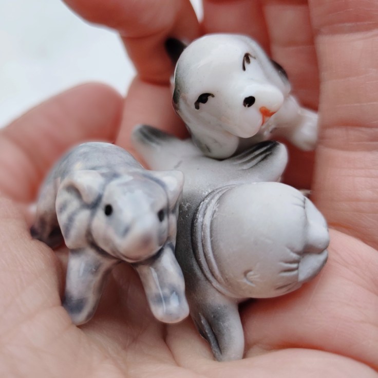 Pieniä keramiikkafiguureja kämmenellä: norsu, hylje ja koira.