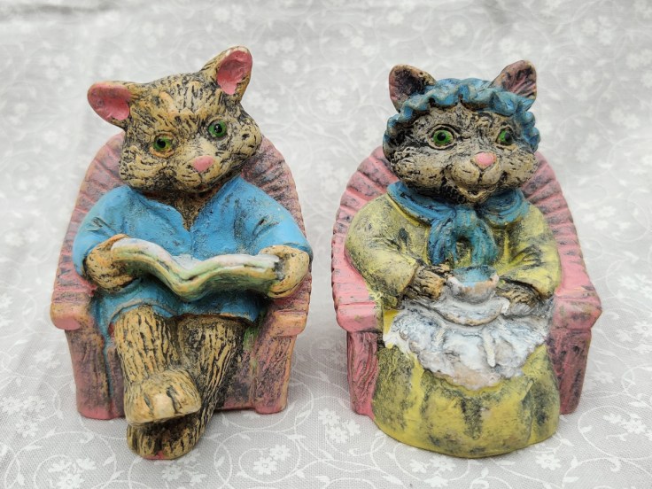 Kaksi tuolissa istuvaa kissafiguuria.