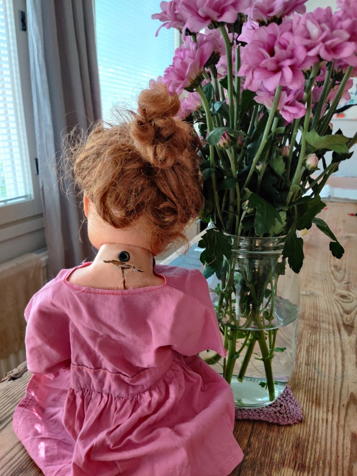 Ideal Doll nukke 1960-luvulta, selkäpuoli. Nukke istuu pöydällä. Nuken vieressä on kukkakimppu.