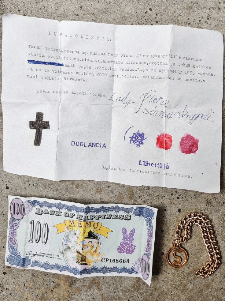 Paperi, jossa on mekaanisella kirjoituskoneella kirjoitettu teksti “Lupatodistus”, leikkiraha ja leikkikoru 1990-luvulta.